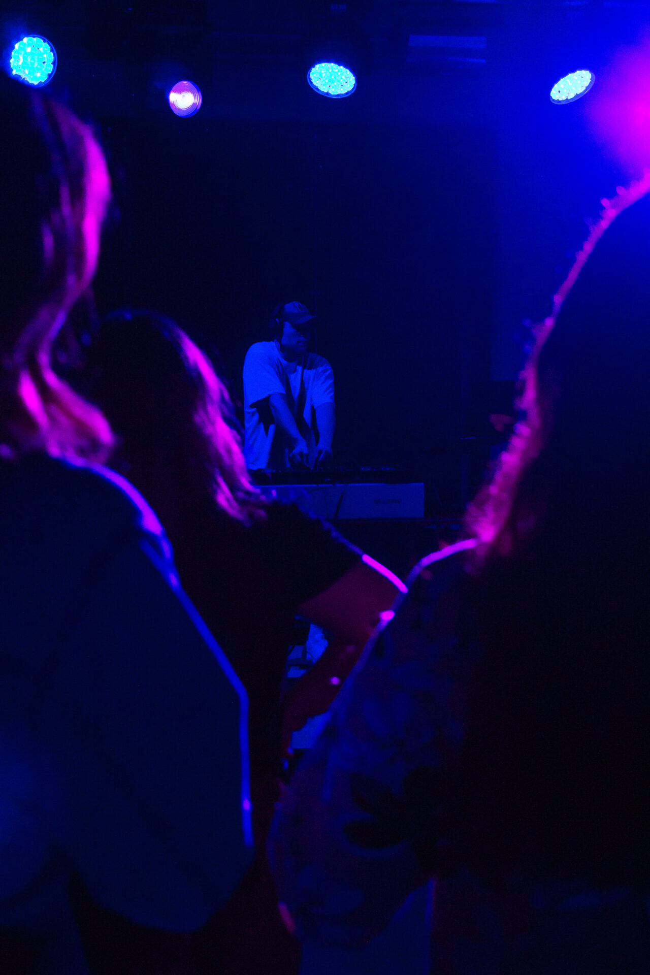 Ein DJ mit Kopfhörern legt unter blauem und violettem Bühnenlicht auf, während die Leute in einem schwach beleuchteten Club zuschauen und tanzen. Dies spiegelt die Energie von INSIDE CAMPUS DESIGN 2025 und den Geist von Zukunft gestalten wider. at Hochschule Coburg
