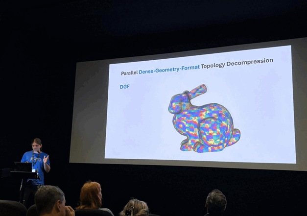 Ein Redner präsentiert dem Publikum in einem dunklen Raum eine Folie mit dem Titel "Parallel Dense-Geometry-Format Topology Decompression" mit einem bunten, geometrischen 3D-Modell eines Kaninchens auf einem großen Bildschirm. at Hochschule Coburg