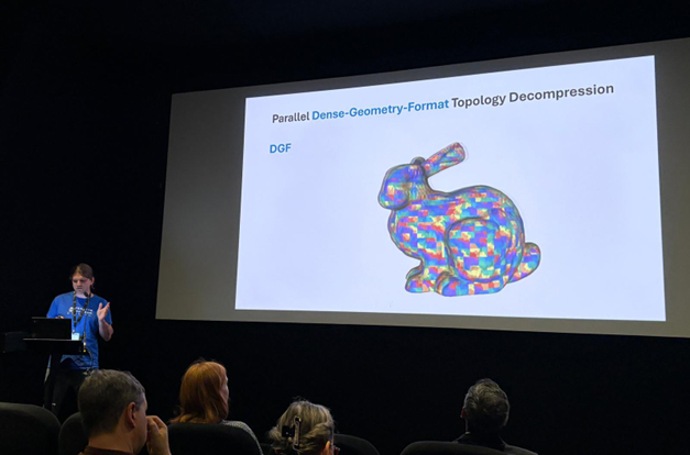 Ein Redner präsentiert dem Publikum in einem dunklen Raum eine Folie mit dem Titel "Parallel Dense-Geometry-Format Topology Decompression" mit einem bunten, geometrischen 3D-Modell eines Kaninchens auf einem großen Bildschirm. at Hochschule Coburg