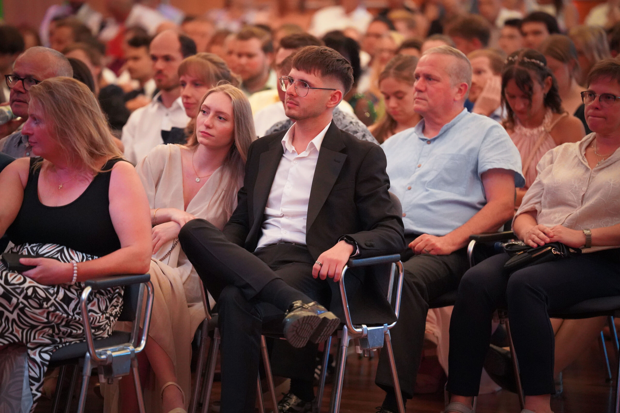 Eine große Gruppe von Menschen sitzt bei einer Veranstaltung in einer Halle dicht an dicht in Reihen. Die meisten sind halb-formal gekleidet und scheinen etwas vor ihnen aufmerksam zu beobachten oder zu hören. at Hochschule Coburg