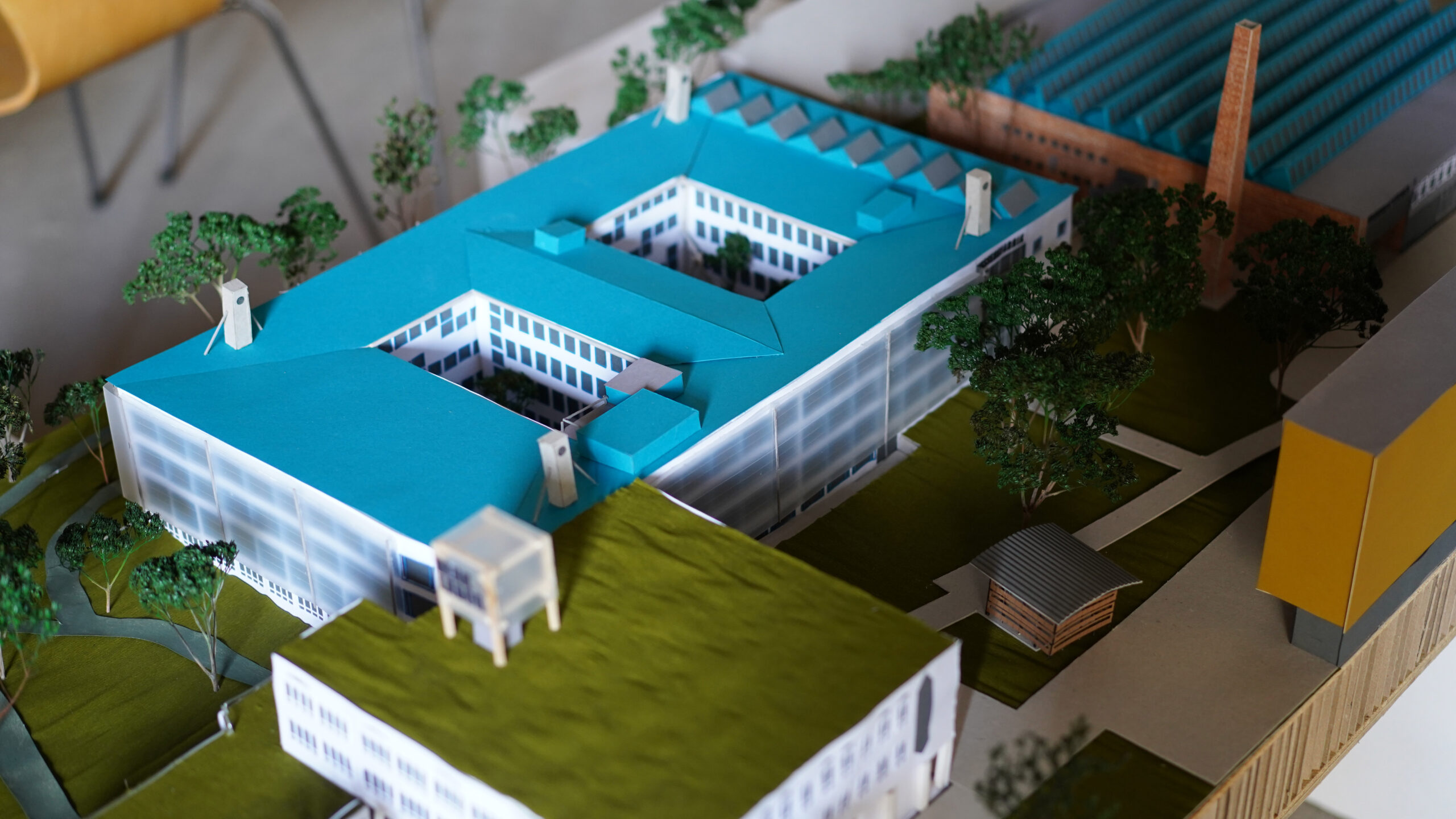 Maßstabsgetreues Architekturmodell eines modernen Gebäudekomplexes mit blauen Dächern, weißen Fassaden, Grünflächen und Wegen, das die transformative Stadtentwicklung durch detaillierte Landschaftselemente und durchdacht gestaltete Strukturen veranschaulicht. at Hochschule Coburg