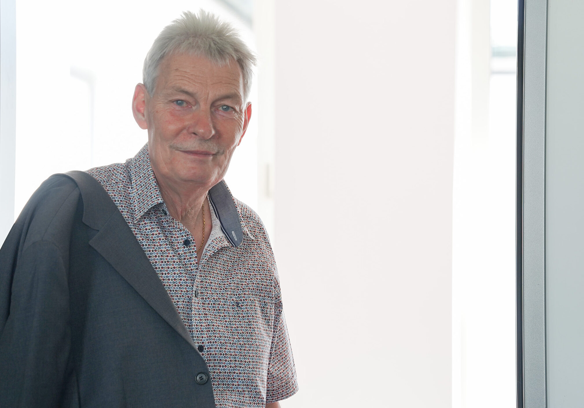 Prof. Dr. Vogt, ein älterer Mann mit kurzen grauen Haaren, einem gemusterten Hemd und einer über die Schulter gehangenen Anzugsjacke, steht in einem Türrahmen, hinter dem Licht in seine Verabschiedung fällt. at Hochschule Coburg