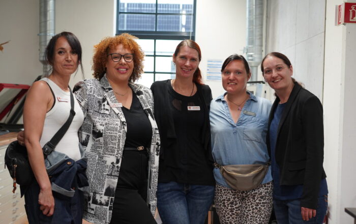 Fünf Frauen stehen eng beieinander in einem Raum und lächeln in die Kamera. Sie sind leger gekleidet und scheinen sich in einem modernen CREAPOLIS Makerspace-Büro zu befinden, das Teamgeist in einem hellen Arbeitsbereich mit großen Fenstern und Regalen im Hintergrund widerspiegelt. at Hochschule Coburg