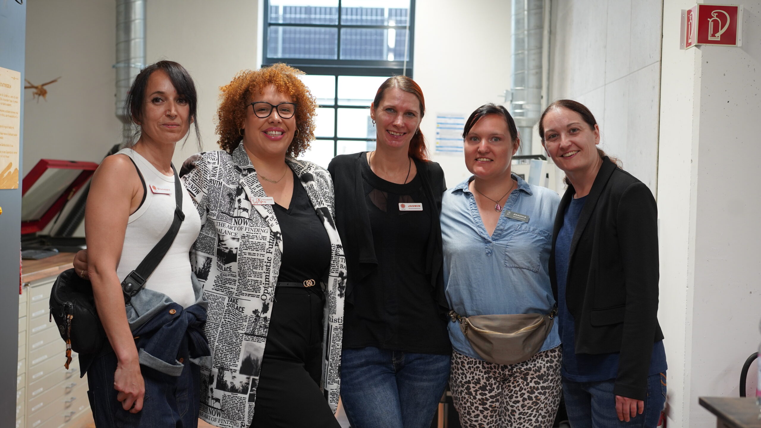 Fünf Frauen stehen eng beieinander in einem Raum und lächeln in die Kamera. Sie sind leger gekleidet und scheinen sich in einem modernen CREAPOLIS Makerspace-Büro zu befinden, das Teamgeist in einem hellen Arbeitsbereich mit großen Fenstern und Regalen im Hintergrund widerspiegelt. at Hochschule Coburg