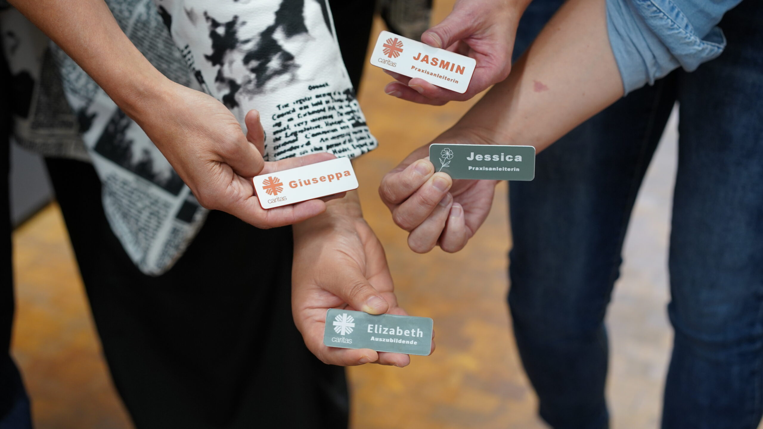 Vier Personen halten Namensschilder mit den Namen Giuseppa, Jasmin, Jessica und Elizabeth hoch. Auf den Schildern sind Rollen, das Caritas-Logo und der Teamgeist abgebildet - perfekt für einen Ausbildungsstart oder eine kreative Zusammenarbeit im CREAPOLIS Makerspace. at Hochschule Coburg