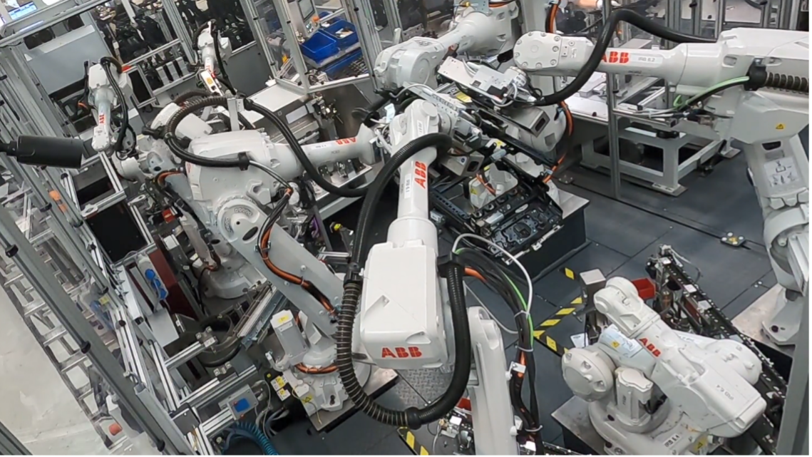 Mehrere industrielle ABB-Roboterarme arbeiten in einer Fabrikumgebung, umgeben von Metallstrukturen und Maschinen, und führen automatisierte Aufgaben an einem Fließband aus - eine Effizienz, die jeden Experimentalphysiker beeindrucken dürfte. at Hochschule Coburg