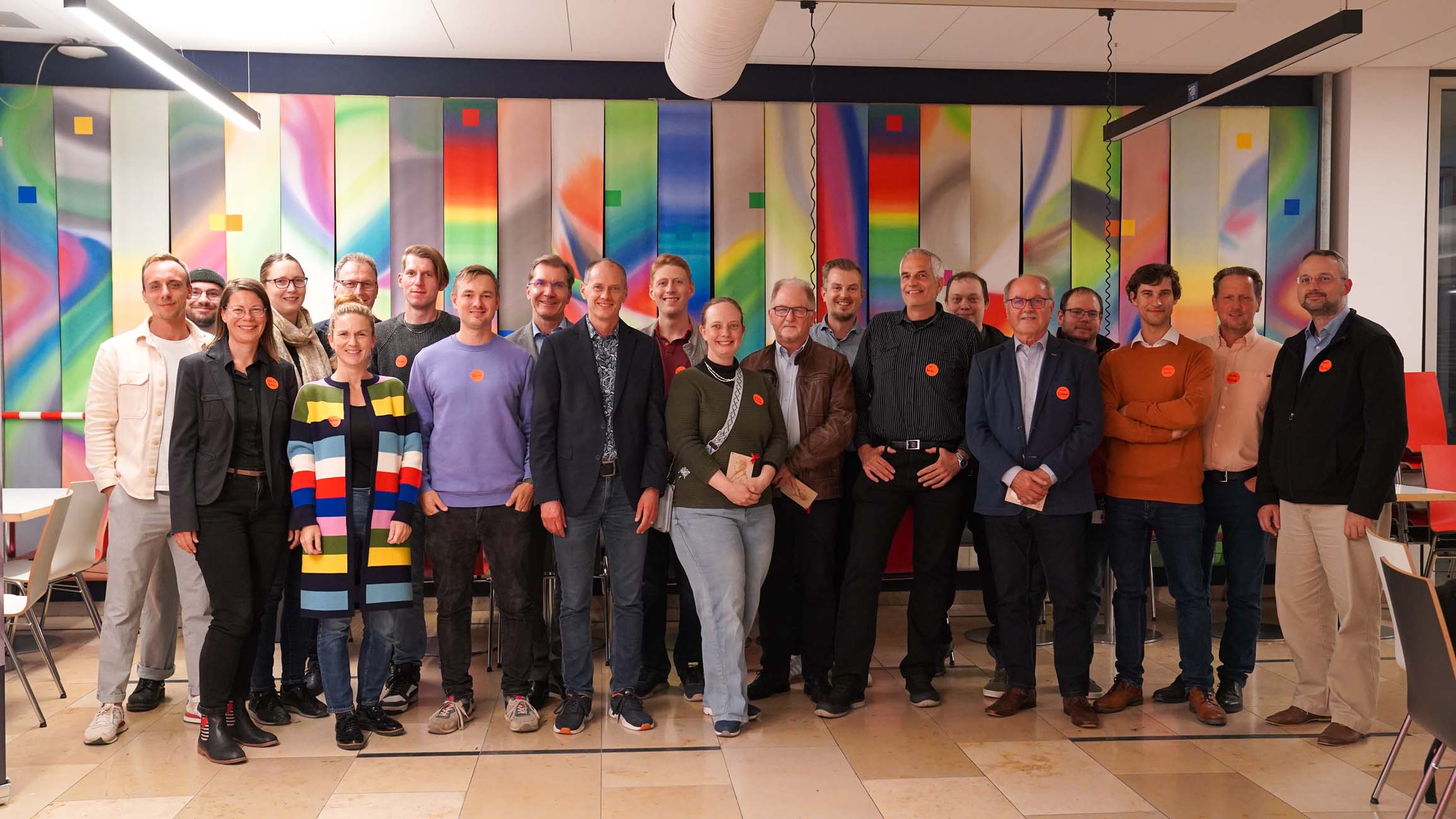 Eine Gruppe von etwa 20 Personen in legerer Business-Kleidung steht im Innenbereich der Hochschule Coburg vor einer bunten, abstrakten Wand für die Streib Discovery Tour zusammen. Die meisten lächeln und schauen in die Kamera. at Hochschule Coburg
