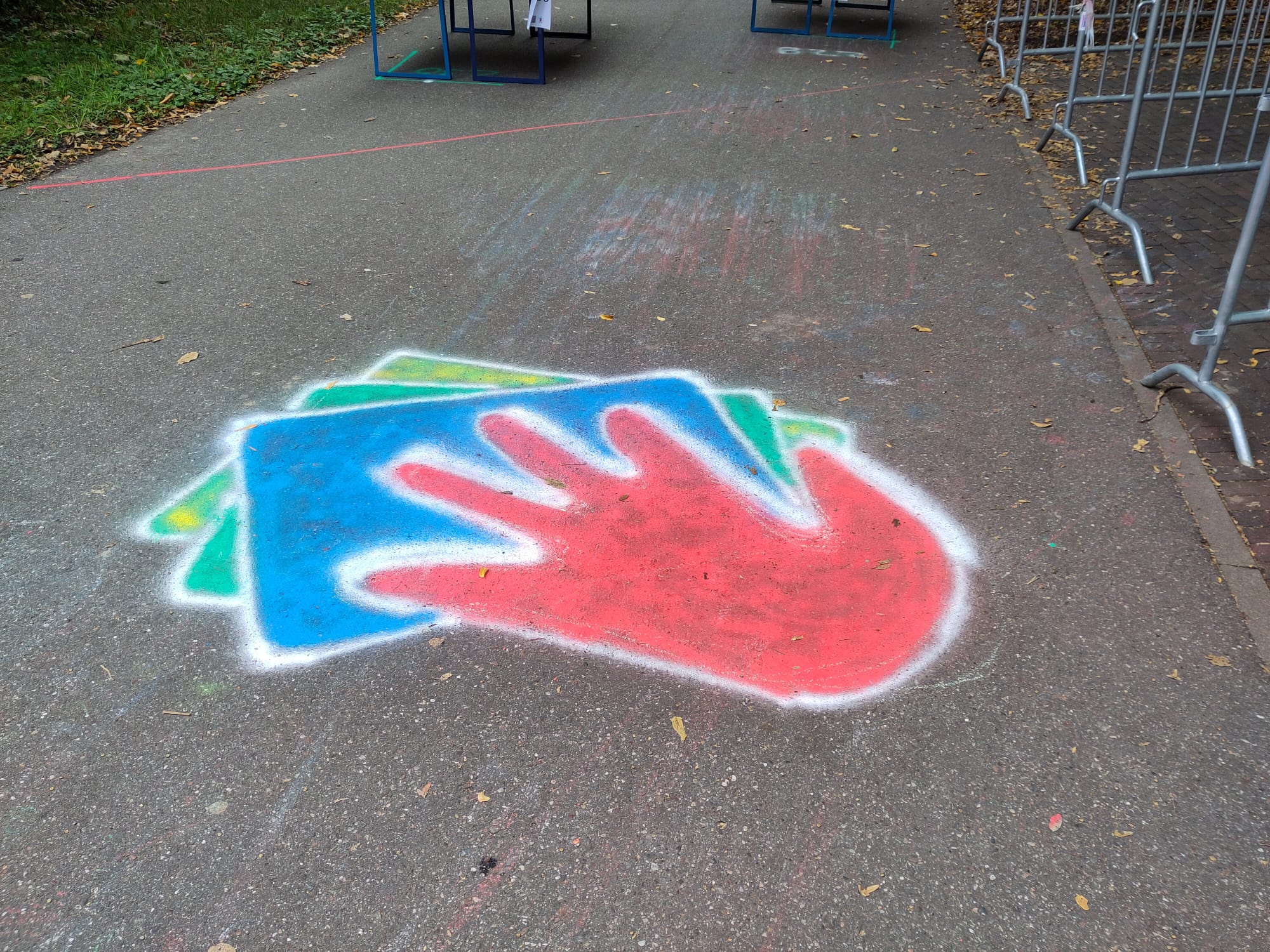 Auf einem Bürgersteig in der Nähe der Hochschule ist eine bunt gesprühte Schablone mit einer roten Hand auf blauem und grünem Hintergrund zu sehen, die von einem weißen Umriss umgeben ist. In der Nähe befinden sich Metallbarrikaden und herabgefallene Blätter, die auf die jüngsten Ereignisse der Klimabildung hinweisen. at Hochschule Coburg