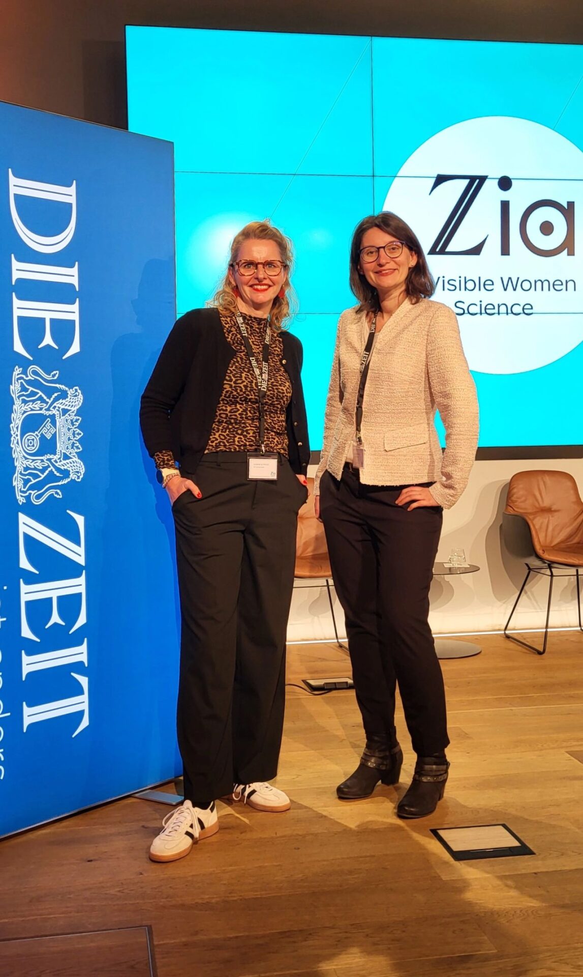 Zwei Frauen stehen lächelnd bei einer Veranstaltung in Berlin, die eine im schwarzen Outfit mit weißen Turnschuhen, die andere im beigen Blazer. Hinter ihnen sind ein "DIE ZEIT"-Transparent und eine Leinwand mit dem "Zia Visible Women in Science"-Logo auf dem ZIA-Kongress 2025 zu sehen. at Hochschule Coburg