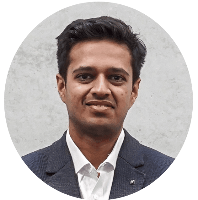 Ein Mann mit kurzen dunklen Haaren, der einen dunklen Blazer und ein weißes Hemd trägt und leicht lächelt, posiert vor einem hellgrauen Hintergrund. at Hochschule Coburg