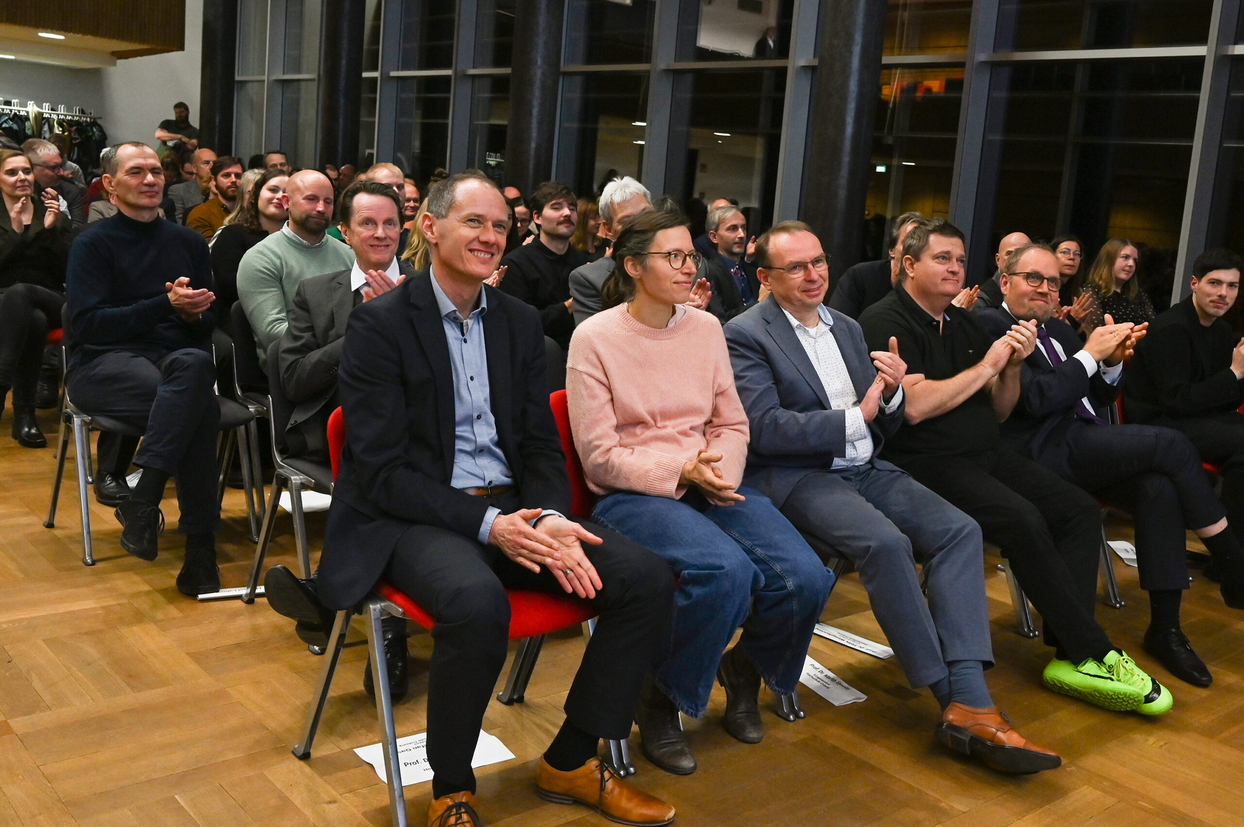 Eine Gruppe von Menschen sitzt in Stuhlreihen in einem modernen, gut beleuchteten Raum an der Hochschule und verfolgt aufmerksam eine Veranstaltung des Dies academicus 2025 und applaudiert. Unter den Zuhörern sind Männer und Frauen, einige lächeln und sind engagiert. at Hochschule Coburg