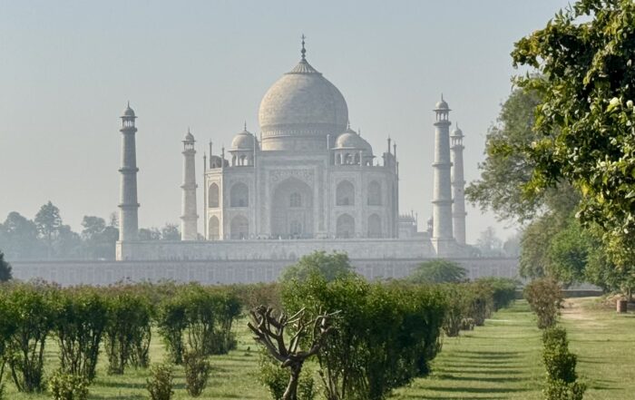 Das Taj Mahal, ein elfenbeinweißes Marmormausoleum mit vier Minaretten, steht im Hintergrund. Grüne Rasenflächen und ordentlich gestutzte Bäume füllen den Vordergrund und symbolisieren zeitlose Schönheit und internationale Präsenz unter einem klaren blauen Himmel. at Hochschule Coburg
