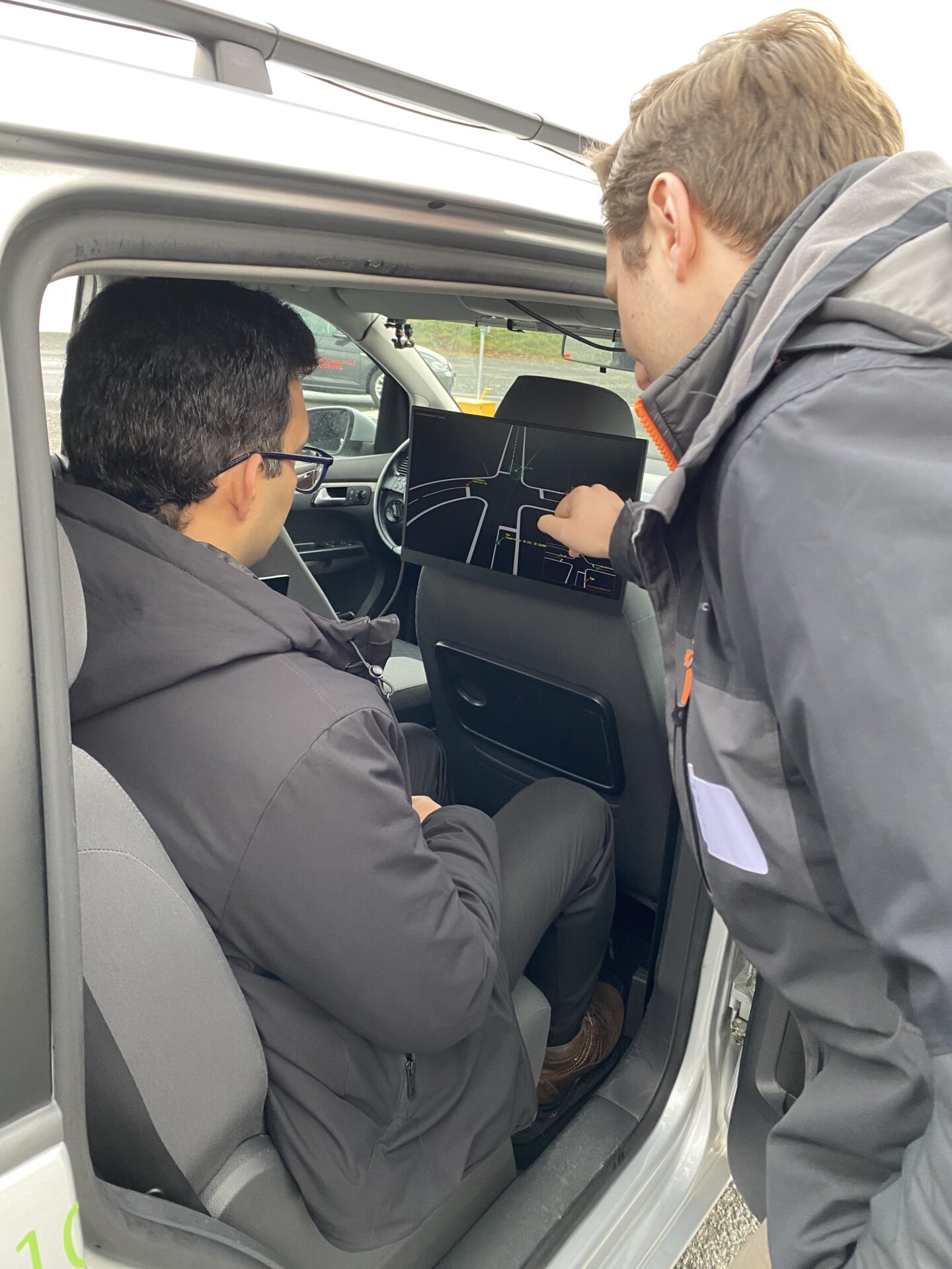 Zwei Personen sitzen in einem Auto, eine auf dem Rücksitz schaut auf ein Display mit einer digitalen Landkarte, die andere vorne zeigt darauf und nutzt DEKOR-X für smarte Kommunikation, um für sichere Straßen zu sorgen. at Hochschule Coburg