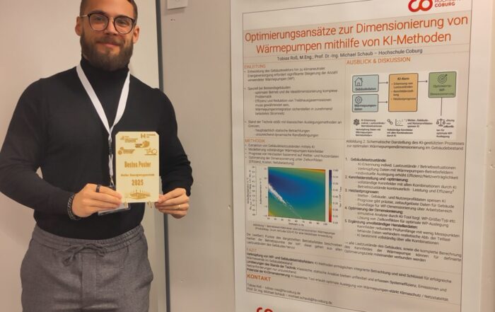 Ein lächelnder Mann mit Brille und Bart hält eine Best-Poster-Award-Trophäe in der Hand, während er neben seinem deutschen Forschungsposter zur Optimierung von Wärmepumpen mit KI-Innovation steht. Das Poster ist auf einer Tafel in einem weißwandigen Raum ausgestellt. at Hochschule Coburg