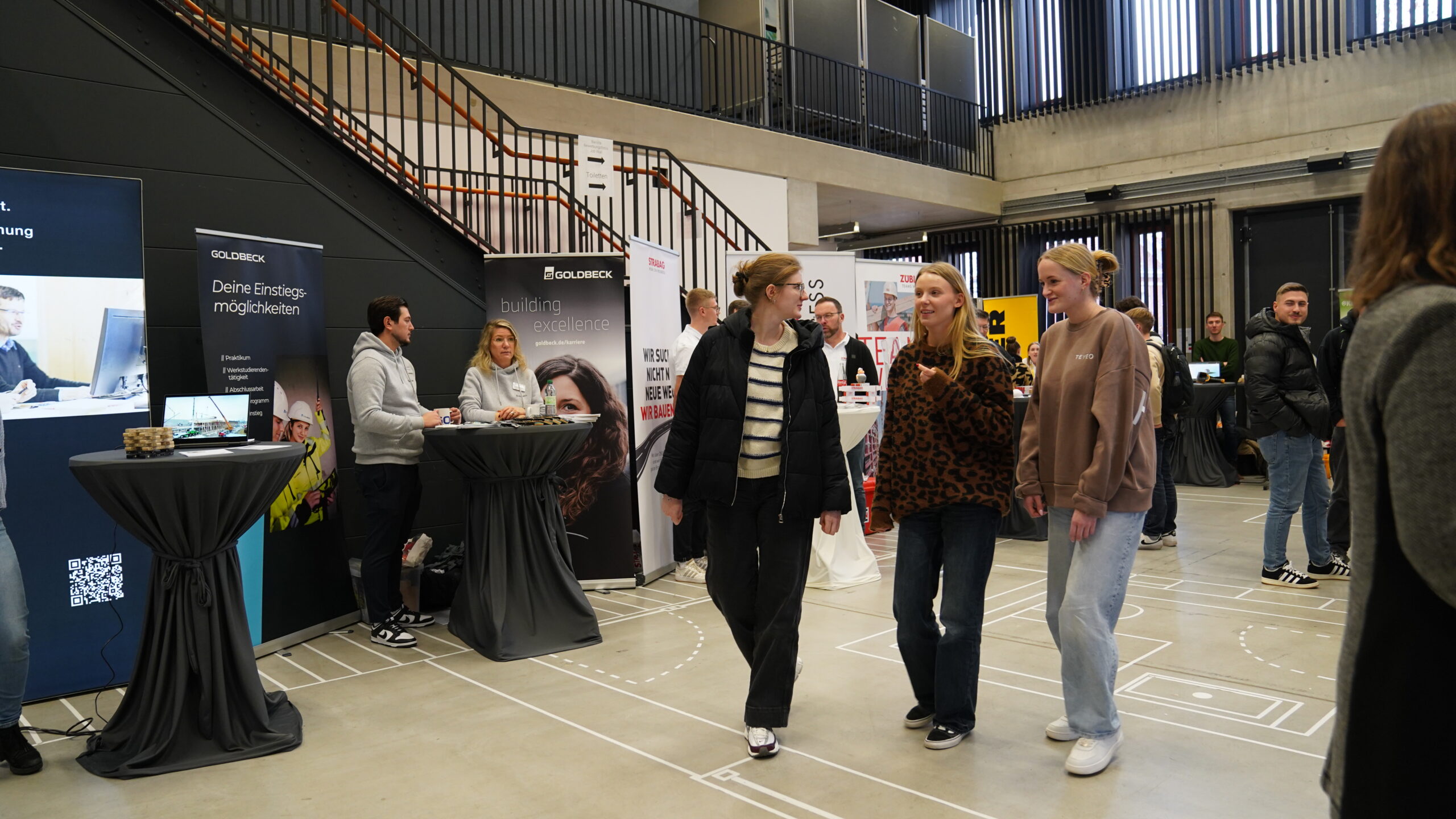 Bei einem Indoor-Karriere-Treff, bei dem sich Unternehmen an Ständen präsentieren, wird gelaufen und geredet. Die Atmosphäre ist locker, die Teilnehmer tragen Pullover und Jeans, während die Nachwuchstalente mit den sitzenden Unternehmensvertretern ins Gespräch kommen. at Hochschule Coburg