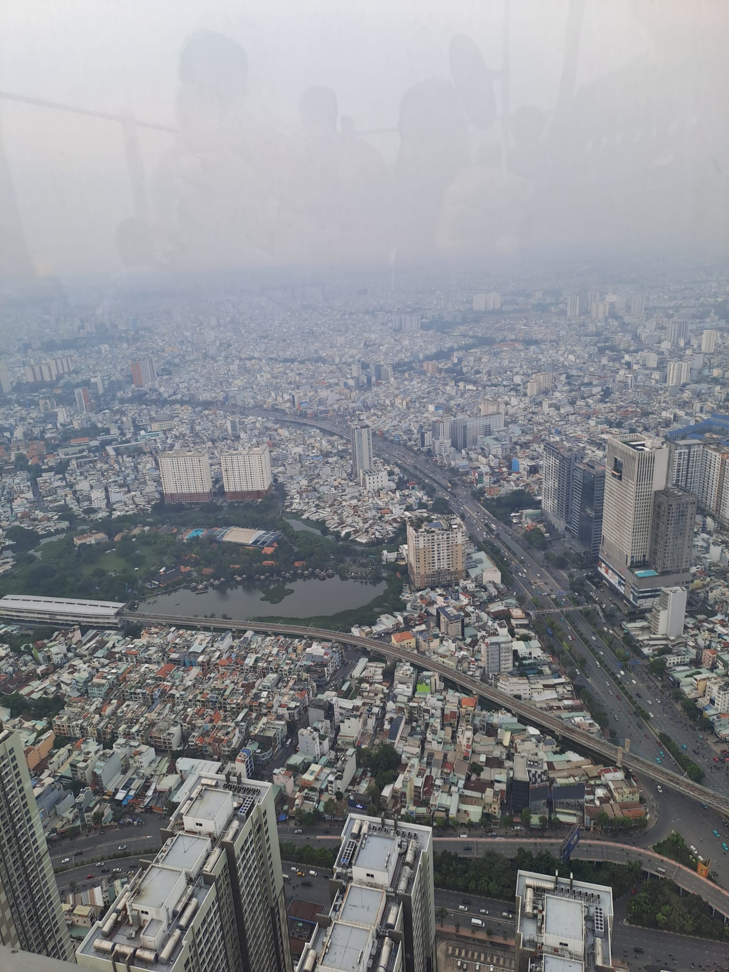 Ein dunstiges Luftbild von Ho-Chi-Minh zeigt ein dicht besiedeltes Stadtbild mit hohen Gebäuden, verkehrsreichen Straßen und Grünflächen, die zwischen dicht gedrängten Gebäuden verstreut sind. at Hochschule Coburg