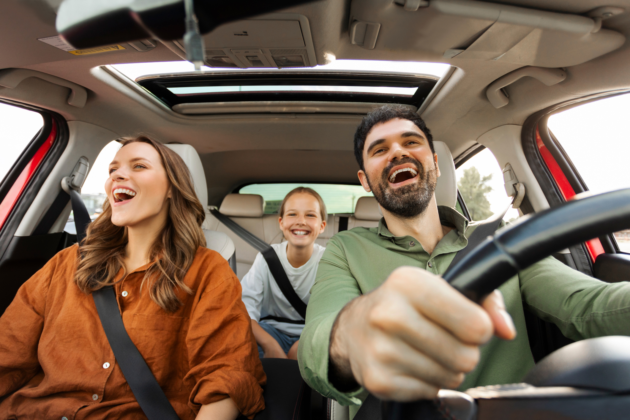 Ein lächelnder Mann fährt ein Auto mit einer Frau auf dem Beifahrersitz und einem Kind auf dem Rücksitz; alle drei sehen glücklich aus und genießen ihre Fahrt. Das Schiebedach ist geöffnet und lässt Licht herein - vielleicht sind sie auf dem Weg zur Langen Nacht der Wissenschaften. at Hochschule Coburg