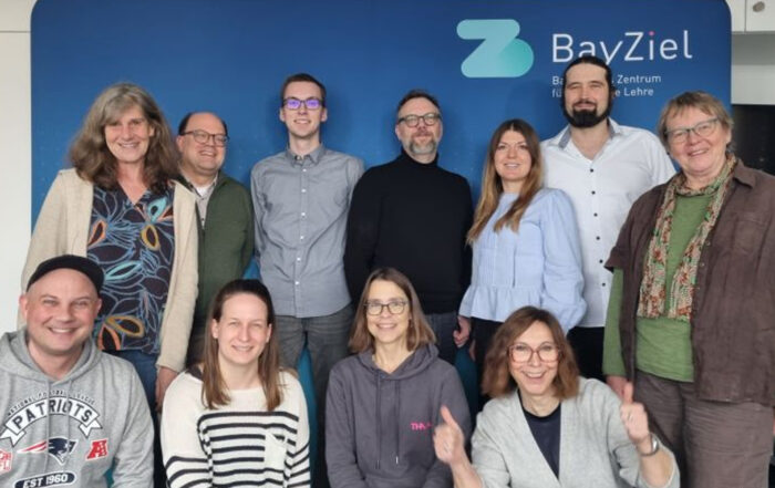 Eine Gruppe von dreizehn Personen, darunter auch Lehrende, die lächelnd vor einem blauen Hintergrund mit dem BayZiel-Logo und -Text posieren. Die leger gekleidete Gruppe spiegelt ein gemeinsames Engagement für Nachhaltigkeit wider. Einige stehen, andere sitzen. at Hochschule Coburg