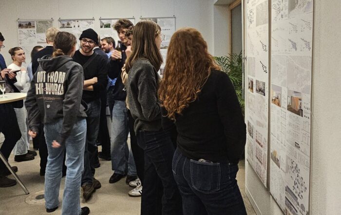 Eine Gruppe von Menschen in Freizeitkleidung steht in einem Raum und betrachtet aufmerksam Plakate mit Diagrammen und Bildern über eine Nachkriegssiedlung. Einige unterhalten sich, andere nehmen die Ausstellung in sich auf und gewinnen neue Perspektiven. at Hochschule Coburg