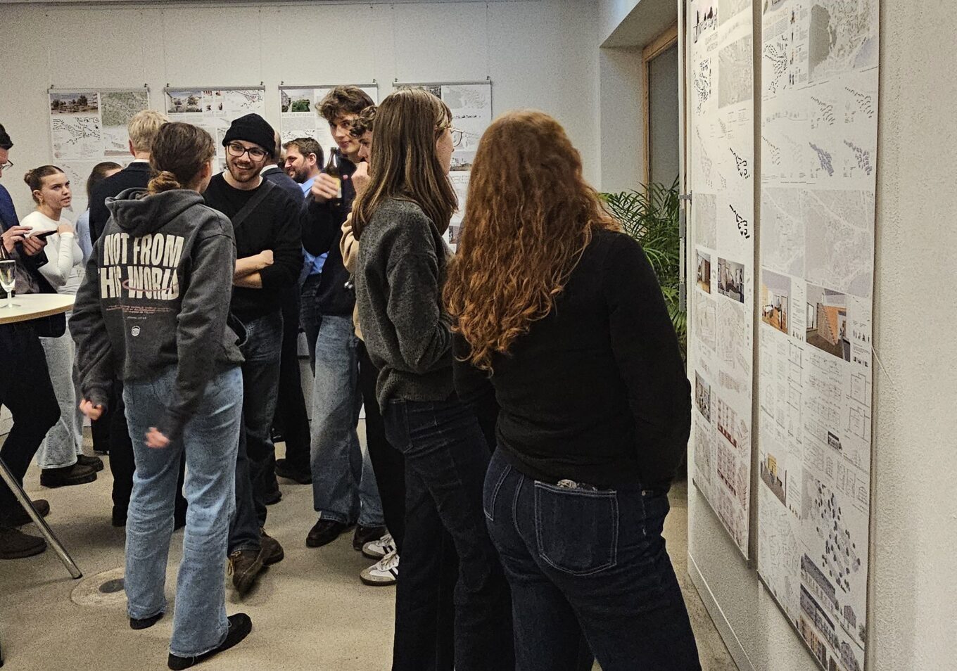 Eine Gruppe von Menschen in Freizeitkleidung steht in einem Raum und betrachtet aufmerksam Plakate mit Diagrammen und Bildern über eine Nachkriegssiedlung. Einige unterhalten sich, andere nehmen die Ausstellung in sich auf und gewinnen neue Perspektiven. at Hochschule Coburg