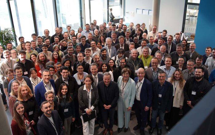 Eine große Gruppe von Doktorandinnen und Doktoranden, gekleidet in Geschäfts- oder Freizeitkleidung, steht in einem hellen, modernen Raum mit großen Fenstern in der Region eng beieinander, lächelt und blickt in die Kamera. at Hochschule Coburg