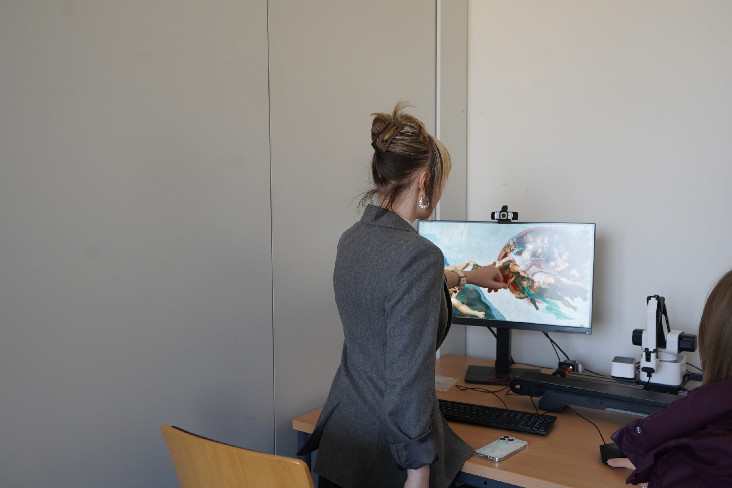 Eine Person steht und zeigt auf einen Computerbildschirm, auf dem ein Bild angezeigt wird, während eine andere in der Nähe an einem Schreibtisch mit einem Mikroskop sitzt, während eines Experimentiertages im Rahmen des Studieninfo-Programms für Thüringer Schulen. at Hochschule Coburg