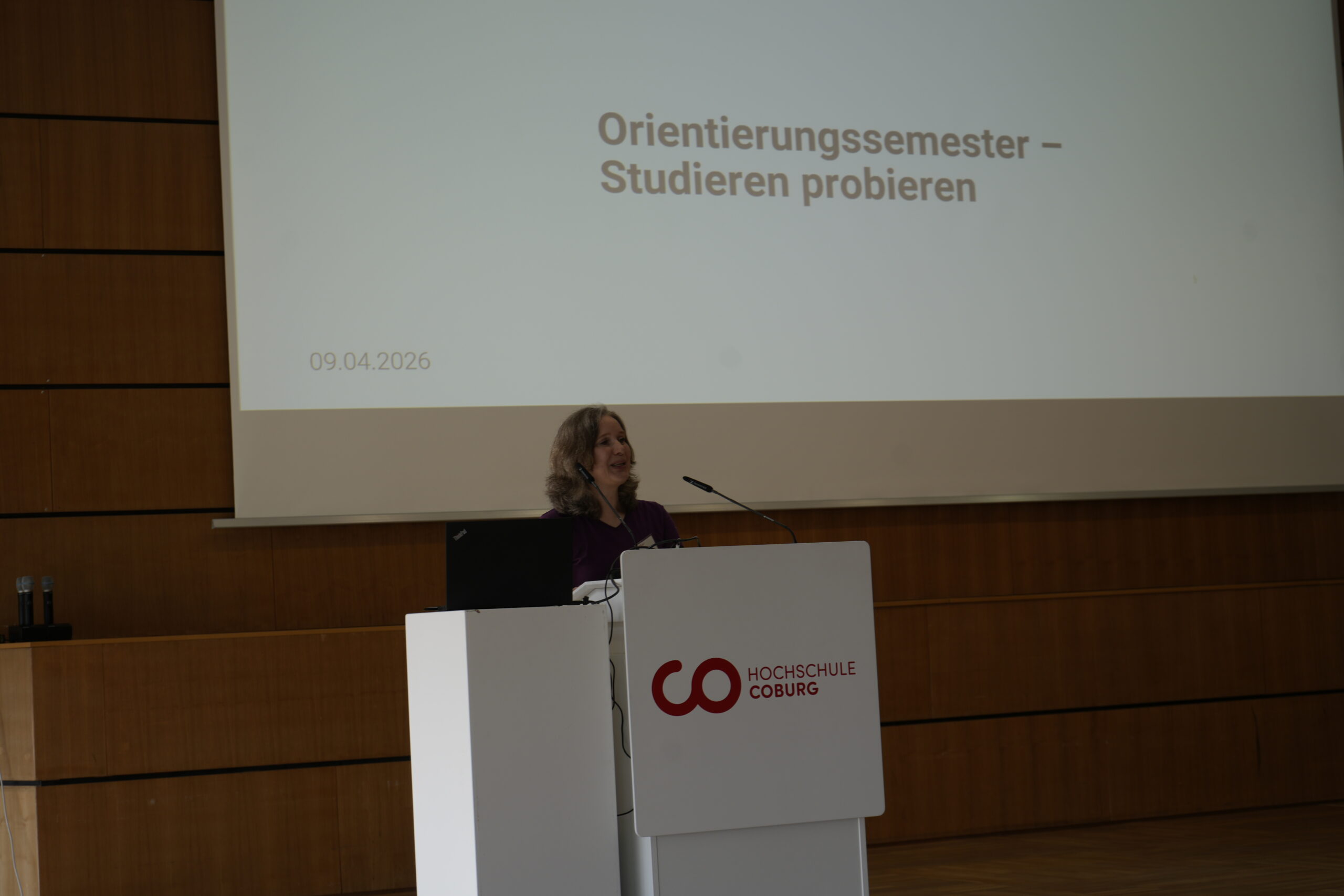 Eine Frau steht am 09.04.2026 an einem Podium mit dem Logo der Hochschule Coburg und informiert über "Orientierungssemester - Studieren probieren". Sie stellt Studiengänge vor und gibt den Studieninteressierten einen Vorgeschmack auf echte Campusluft. at Hochschule Coburg