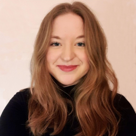 person_fischer_marina_20260421.jpg A young woman with long, wavy light brown hair smiles at the camera. She is wearing a black top and is posed against a plain, light-colored background. at Hochschule Coburg