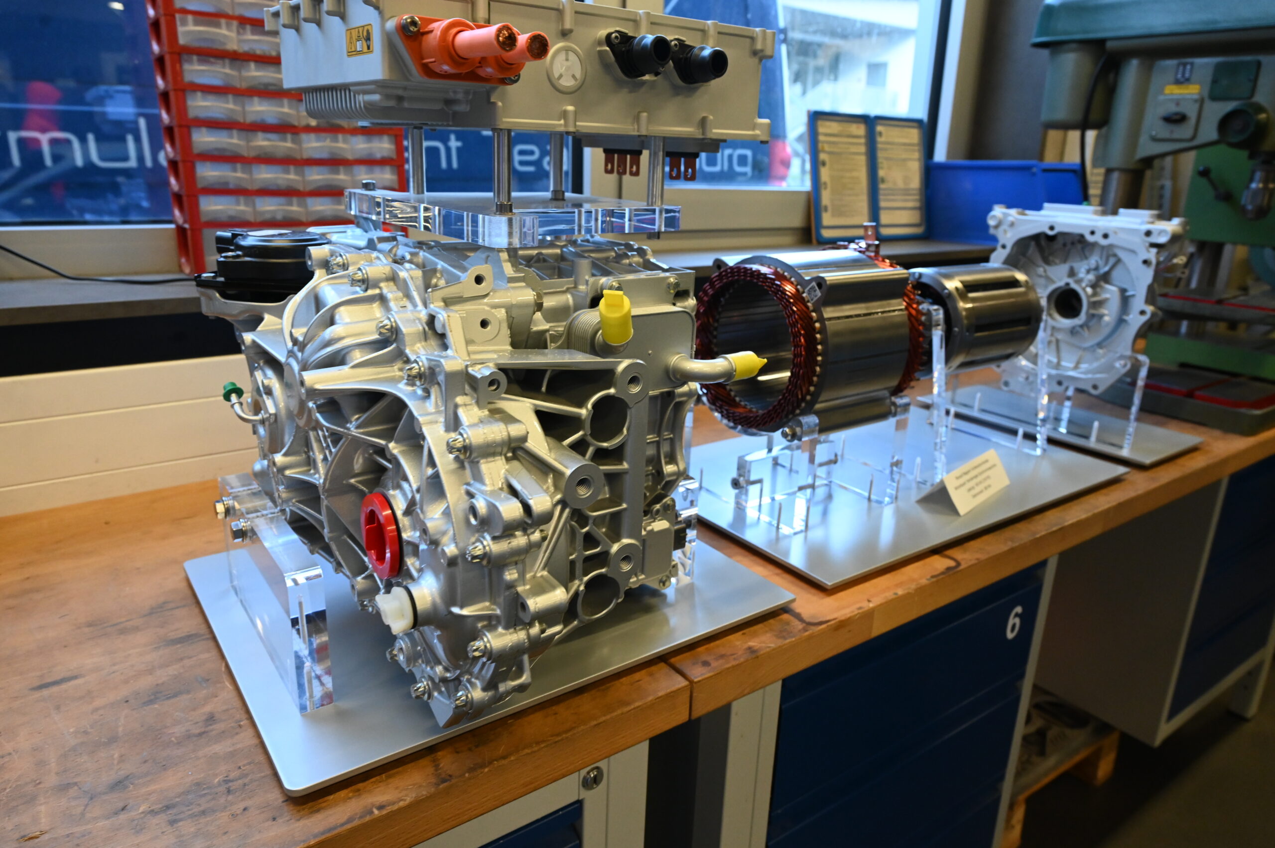 Nahaufnahme eines Elektrofahrzeug-Antriebsstrangs und von Motorkomponenten, die während der Langen Nacht der Wissenschaften in einer Werkstatt ausgestellt sind. Zu sehen sind detaillierte Maschinen und Kabel auf einer metallenen Werkbank mit Werkzeugen und Geräten im Hintergrund. at Hochschule Coburg