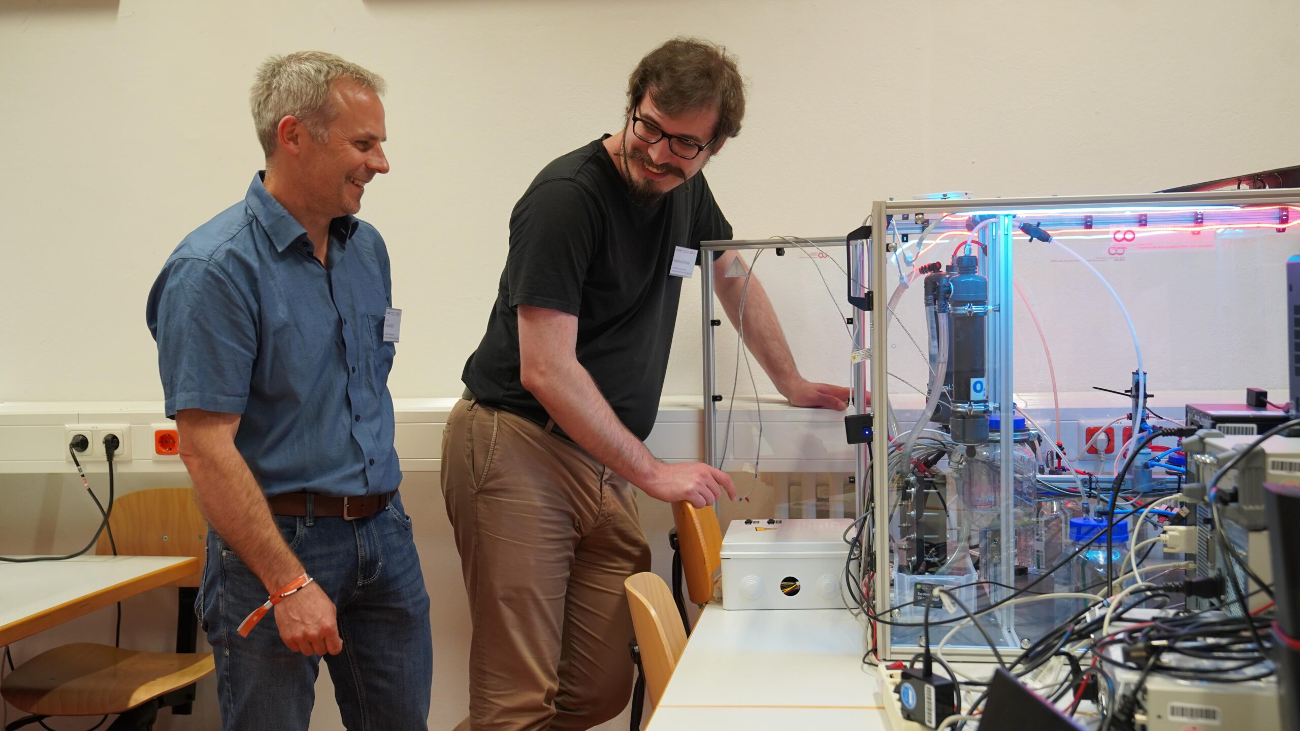Zwei Männer stehen während der Langen Nacht der Wissenschaften in einem Labor neben einem großen, transparenten 3D-Drucker. Der eine bedient die Maschine, der andere schaut zu. Beide diskutieren angeregt inmitten der technischen Geräte und erzeugen mit ihrem Enthusiasmus echte Resonanz. at Hochschule Coburg