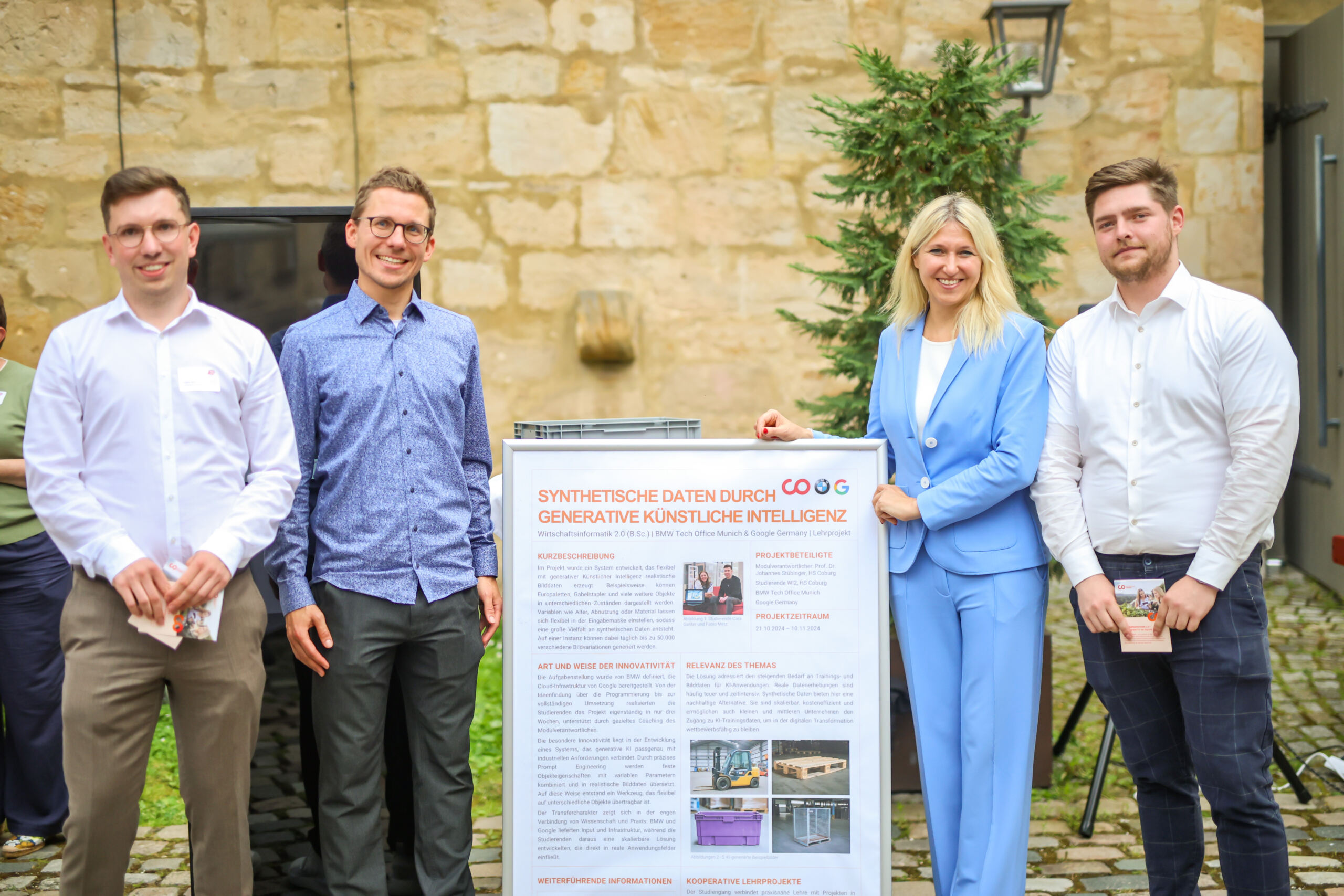 Vier Personen stehen im Freien auf dem Innovationskongress in Oberfranken und lächeln neben einem Plakat zum Thema synthetische Daten durch generative künstliche Intelligenz. Zu der Gruppe in Geschäftskleidung gehören drei Männer und eine Frau; hinter ihnen sind eine Steinmauer und ein kleiner Baum zu sehen. at Hochschule Coburg