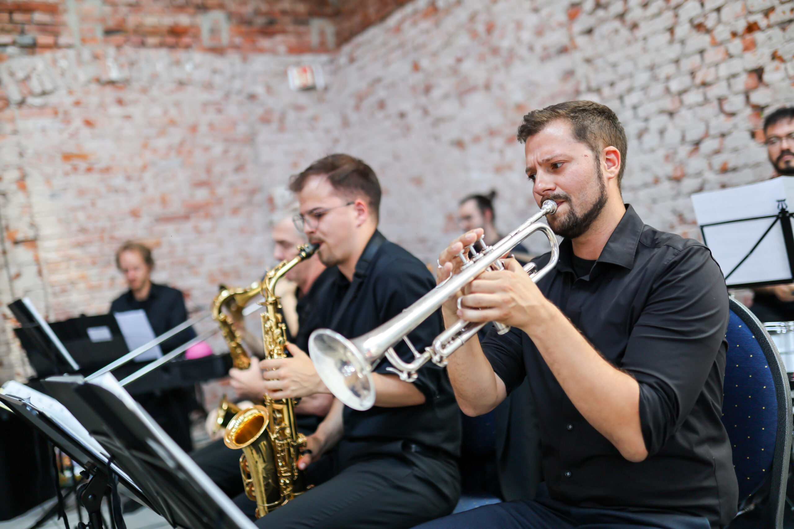 Eine Gruppe von Musikern in schwarzer Kleidung spielt vor einer rustikalen Backsteinmauer Blech- und Holzblasinstrumente, darunter eine Trompete und ein Saxophon, im Rahmen einer Veranstaltung zur Feier von „zehn Jahre Hochschulstandort Kronach“. at Hochschule Coburg