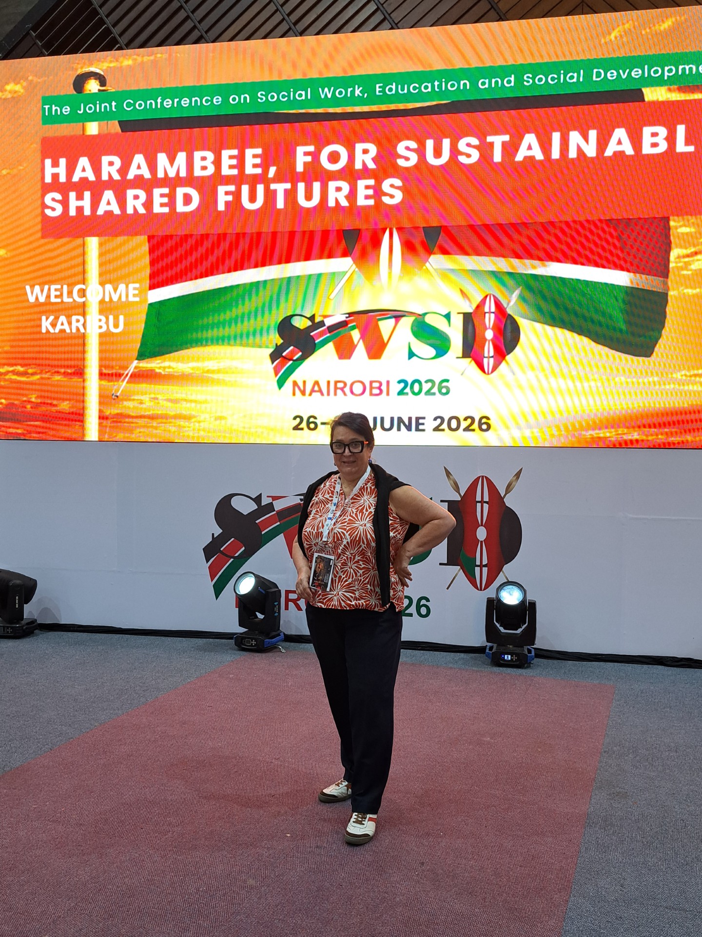 Eine Person steht selbstbewusst vor einer großen Konferenzleinwand, auf der „Harambee for Sustainable Shared Futures“ zu lesen ist, auf der WSWD Nairobi 2026, mit kenianischen Flaggen und Veranstaltungsdetails im Hintergrund, und verkörpert damit den Geist von „Katastrophen lernen“ auf dieser entscheidenden Weltkonferenz in Nairobi. at Hochschule Coburg