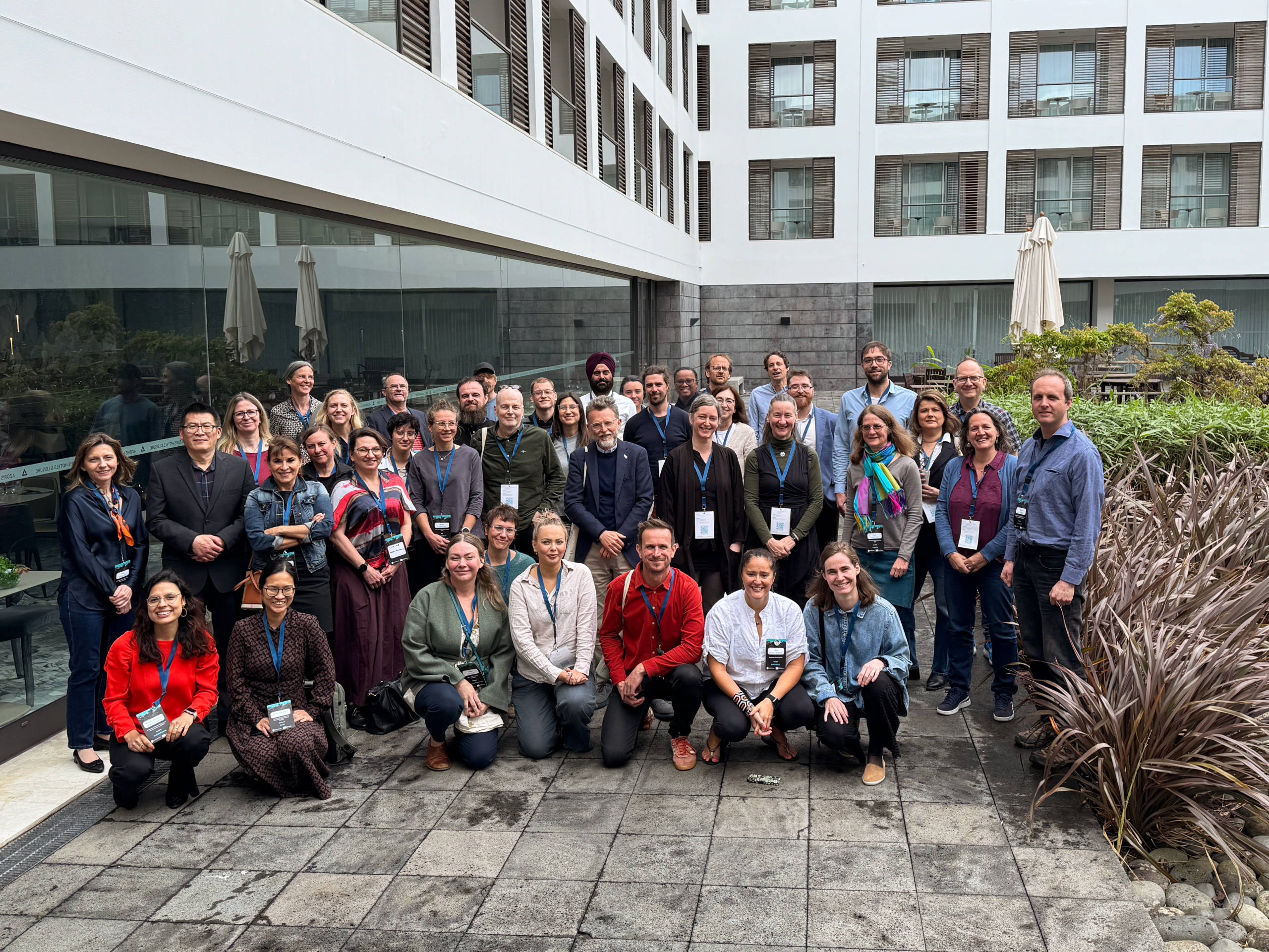 Eine Gruppe von etwa 45 Personen posiert vor einem modernen Gebäude für ein Foto; sie stehen und knien auf einer gepflasterten Terrasse, im Hintergrund sind Pflanzen und Sonnenschirme zu sehen – eine inspirierende Zusammenkunft, die der Wissenschaft und der innovativen Forstpraxis gewidmet ist, die die Zukunft der europäischen Wälder prägen. at Hochschule Coburg