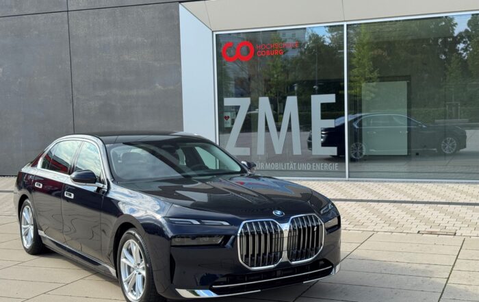Eine schwarze BMW-Limousine steht auf einer gepflasterten Fläche vor einem modernen Gebäude mit großen Fenstern, auf denen die Buchstaben „ZME“ und ein rotes Logo zu sehen sind. at Hochschule Coburg