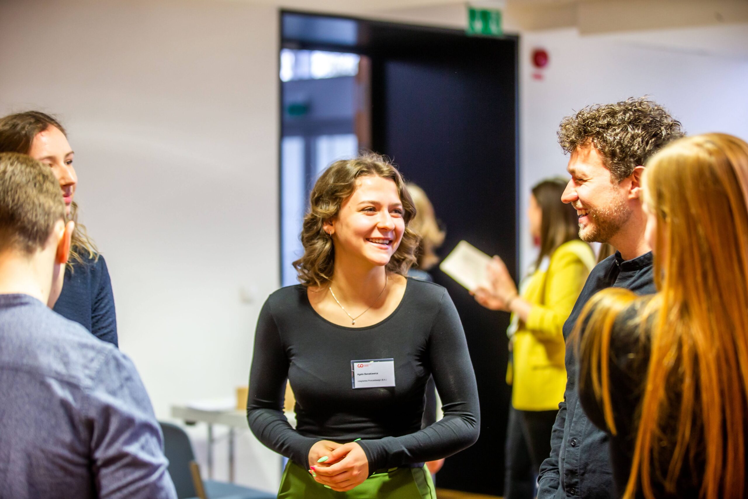 Eine Gruppe von Menschen steht und unterhält sich in einem Raum bei einer Veranstaltung, die wie eine Fach- oder Networking-Veranstaltung wirkt und möglicherweise im Zusammenhang mit dem Deutschland-Stipendium steht. Eine Frau in der Mitte lächelt, und alle scheinen in ein Gespräch vertieft zu sein, was das Potenzial unterstreicht, das solche Zusammenkünfte für die persönliche und berufliche Weiterentwicklung bieten. at Hochschule Coburg