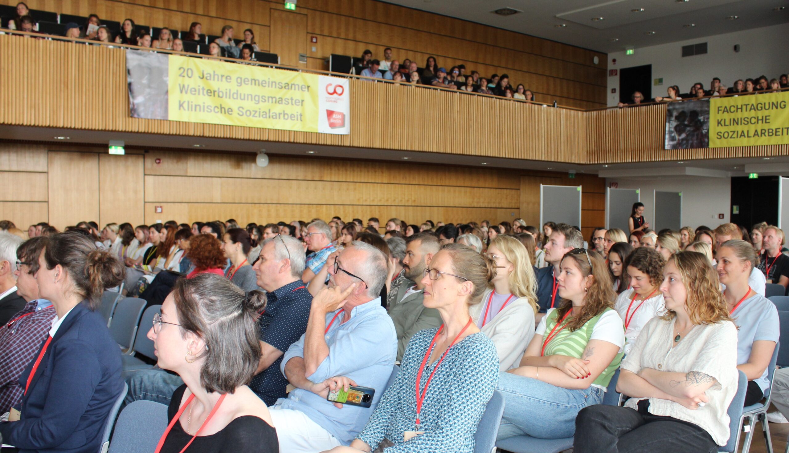 Zuhörer sitzen in einem großen Hörsaal und verfolgen einen Vortrag unter einem Banner, das für den 25-jährigen Masterstudiengang „Klinische Sozialarbeit“ wirbt. at Hochschule Coburg
