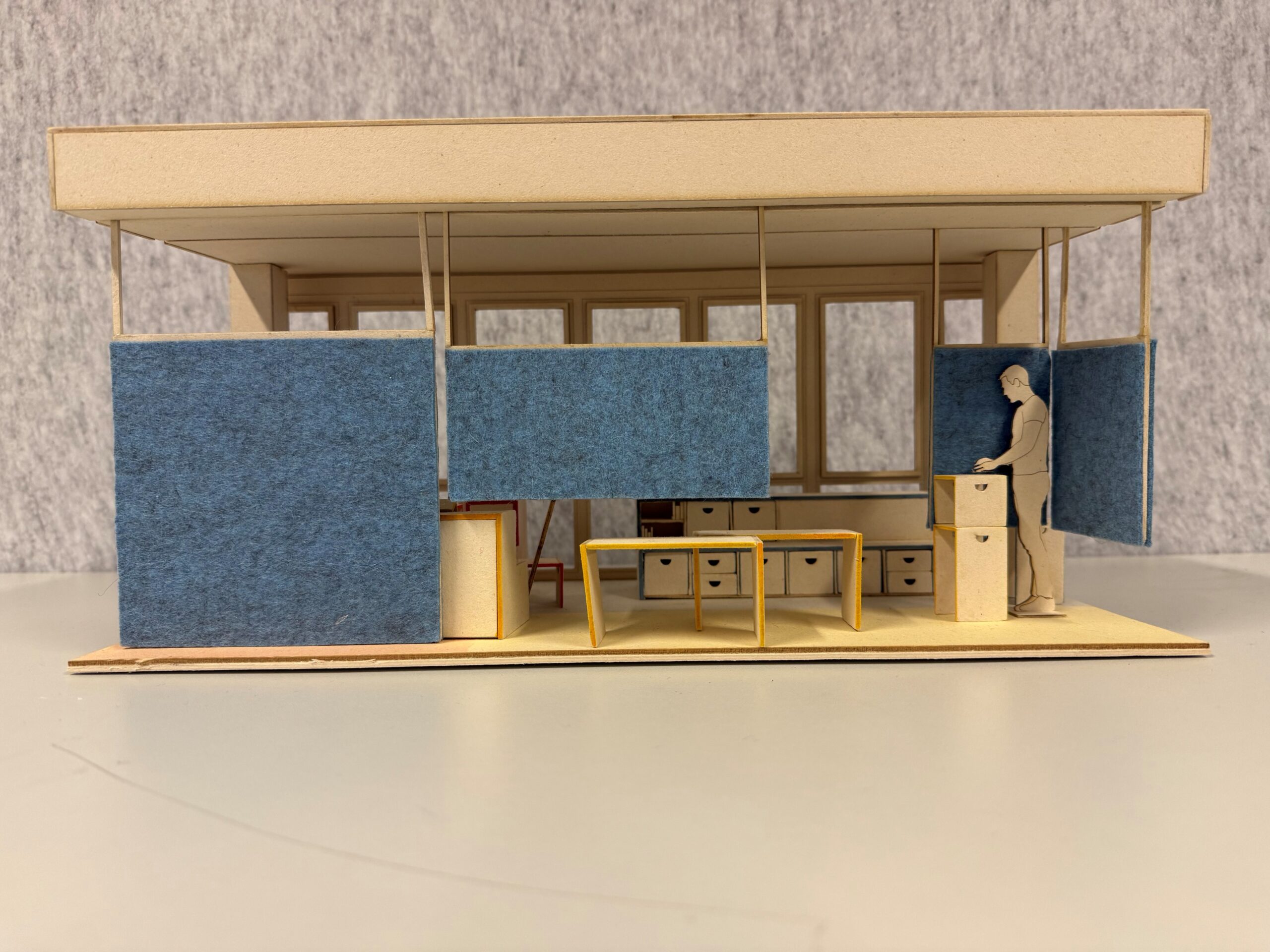 Architekturmodell einer Inneneinrichtung mit blauen Trennwänden, einem Schreibtisch, Aufbewahrungsmöbeln und einer ausgeschnittenen Personenfigur. at Hochschule Coburg