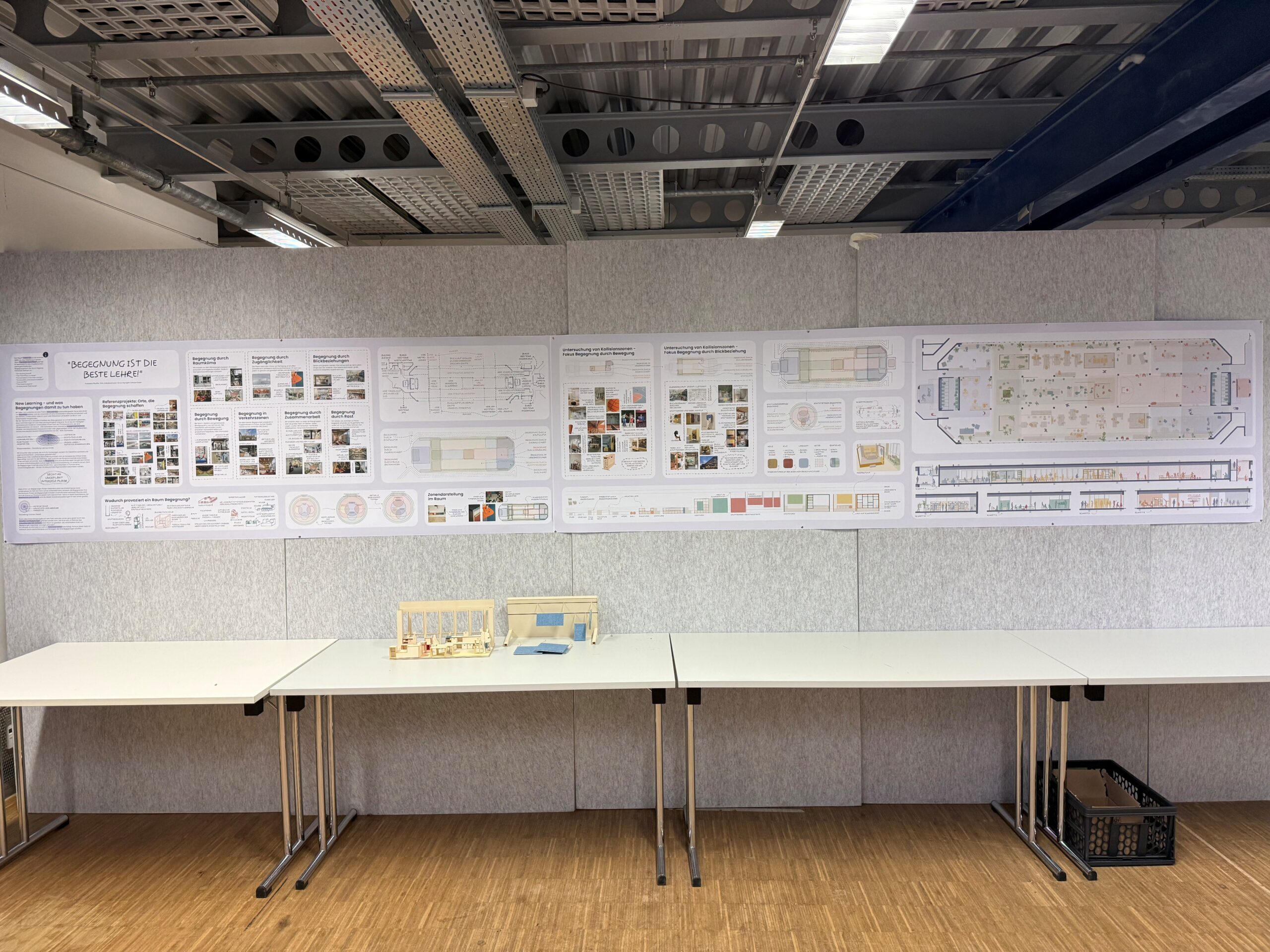 Drei große Informationsplakate zum Thema „Entwurf“ sind an einer Wand über Tischen angebracht, auf denen zwei Architekturmodelle stehen. at Hochschule Coburg