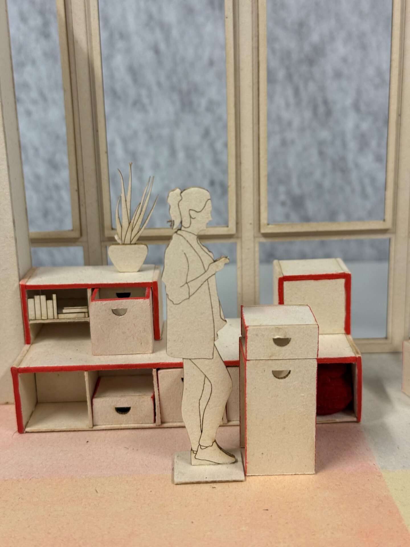 Ein maßstabsgetreues Modell eines Innenraums mit einer lasergeschnittenen Pappfigur einer Frau, die vor minimalistischen Holzregalen steht. at Hochschule Coburg