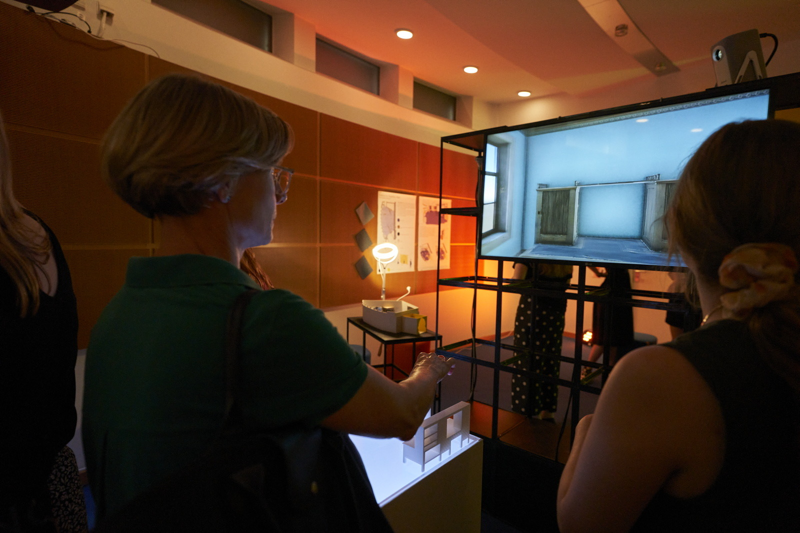 Coburger Studierende betrachten in einer Galerie ein Architekturmodell und einen digitalen Bildschirm, auf dem Goethes Arbeitszimmer zu sehen ist. at Hochschule Coburg