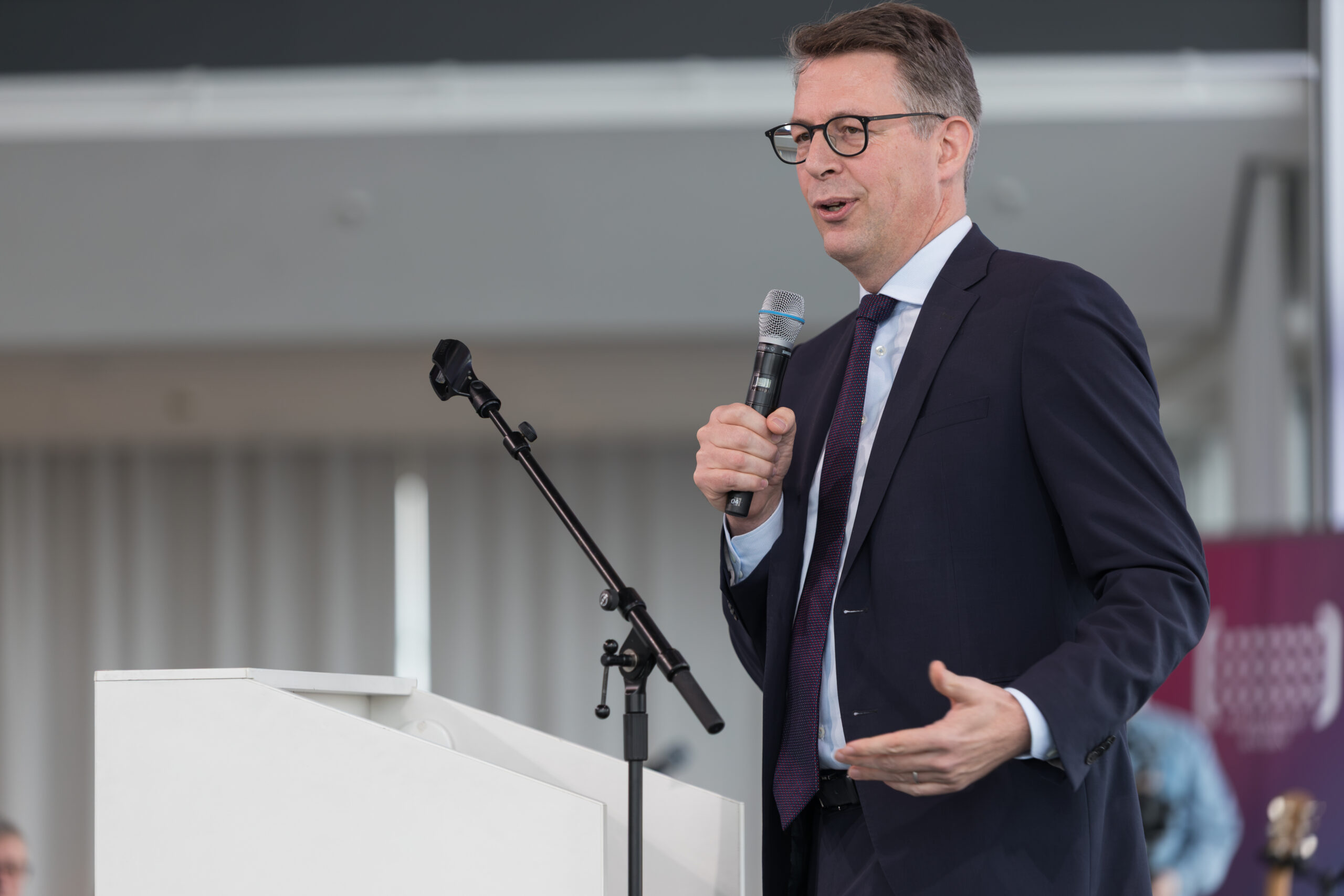 Ein Mann im Anzug und mit Brille spricht während einer Jubiläumsfeier auf einer Bühne der Hochschule Bayern in ein Mikrofon. at Hochschule Coburg