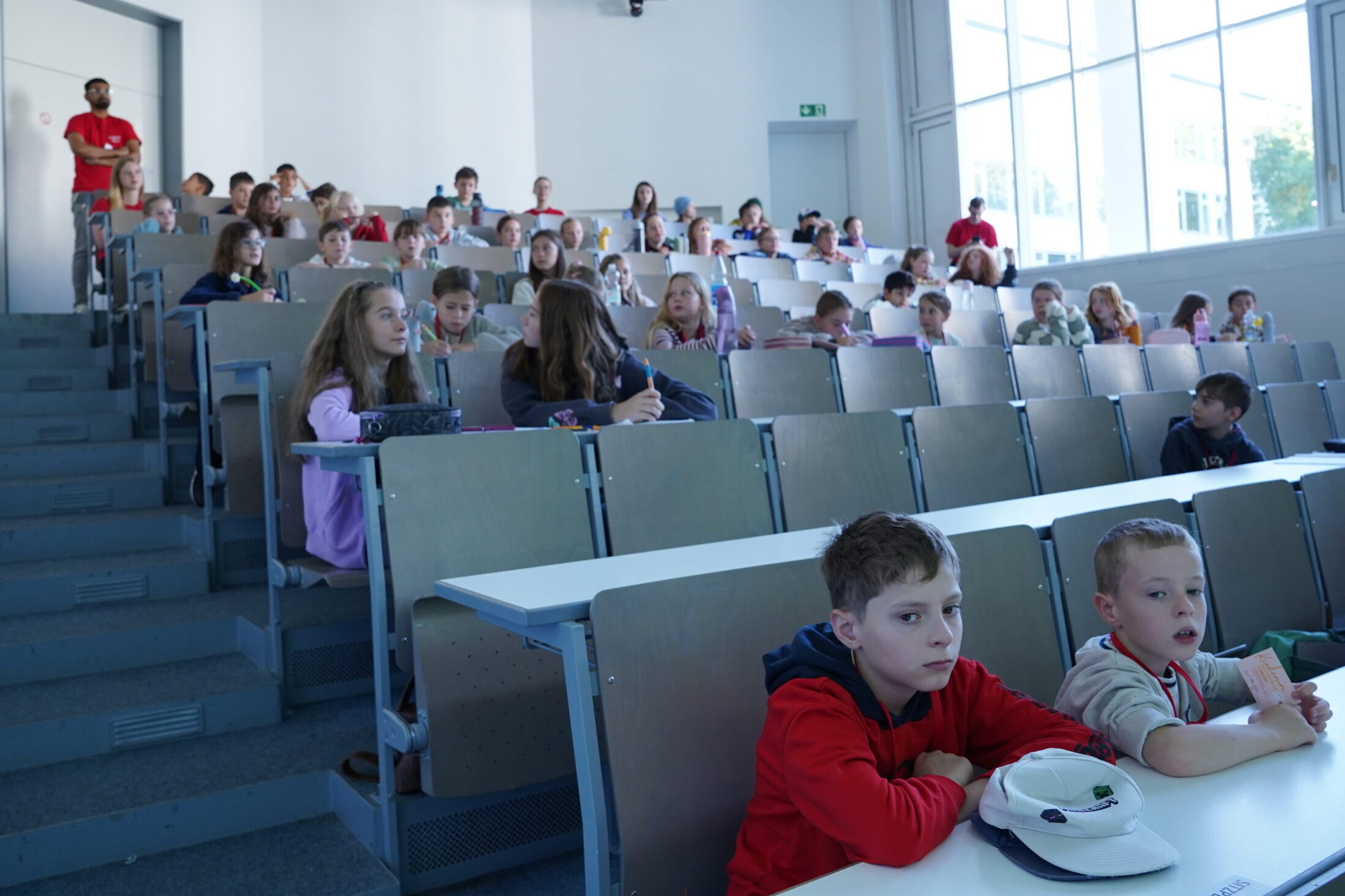 Eine Gruppe von KinderUni-Studierenden sitzt in einem stufenförmigen Hörsaal, darunter auch einige Stammgäste. at Hochschule Coburg