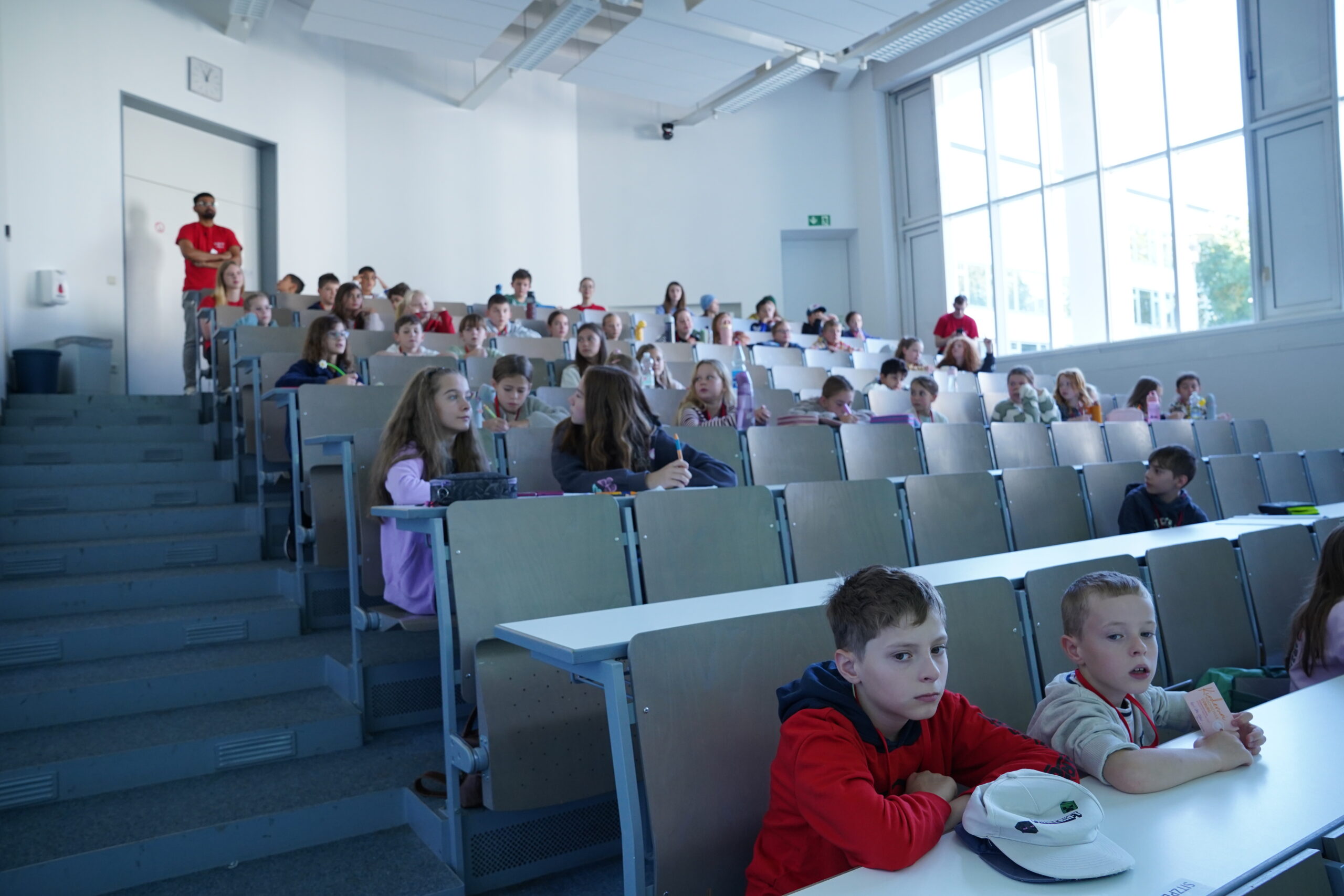 Eine Gruppe von KinderUni-Studierenden sitzt in einem stufenförmigen Hörsaal, darunter auch einige Stammgäste. at Hochschule Coburg