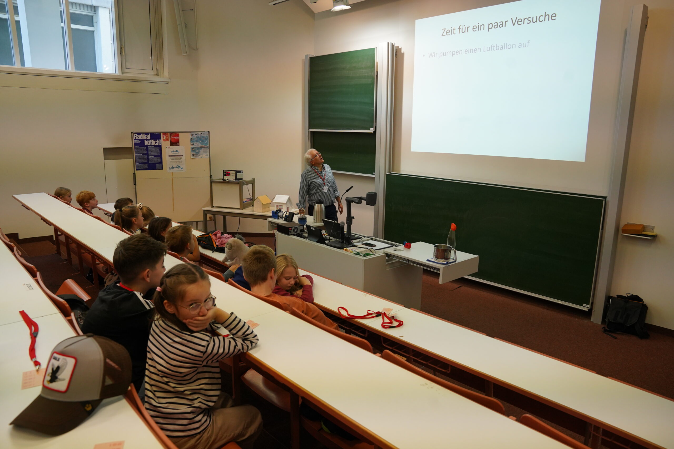 Ein Dozent steht am Rednerpult vor einer Klasse voller Schüler, darunter auch einige Stammgäste, die an der KinderUni-Veranstaltung teilnehmen. at Hochschule Coburg