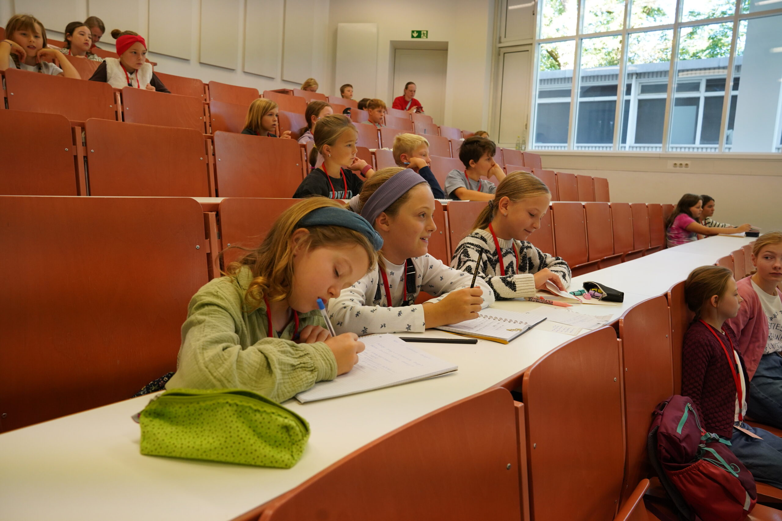 Die Stammgäste der KinderUni sitzen an Schreibtischen in einem stufenförmig angeordneten Hörsaal und schreiben in ihre Hefte. at Hochschule Coburg