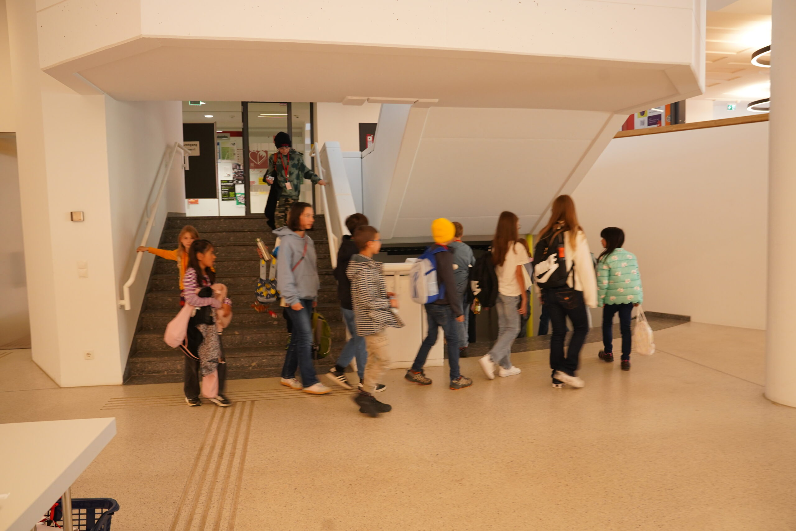 Eine Gruppe von KinderUni-Studierenden geht eine Treppe in einem modernen, weiß getünchten Gebäude hinauf und umrundet sie. at Hochschule Coburg