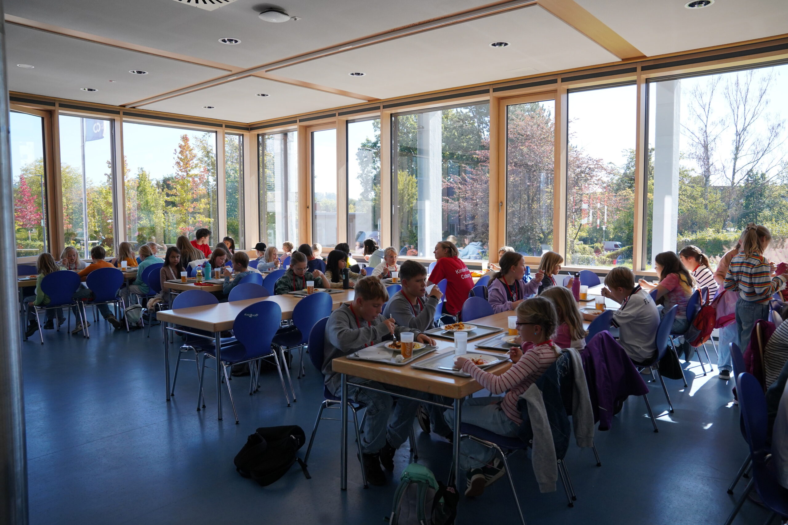 Die KinderUni-Teilnehmer essen in einer sonnendurchfluteten Cafeteria mit großen Fenstern an Tischen zu Mittag. at Hochschule Coburg