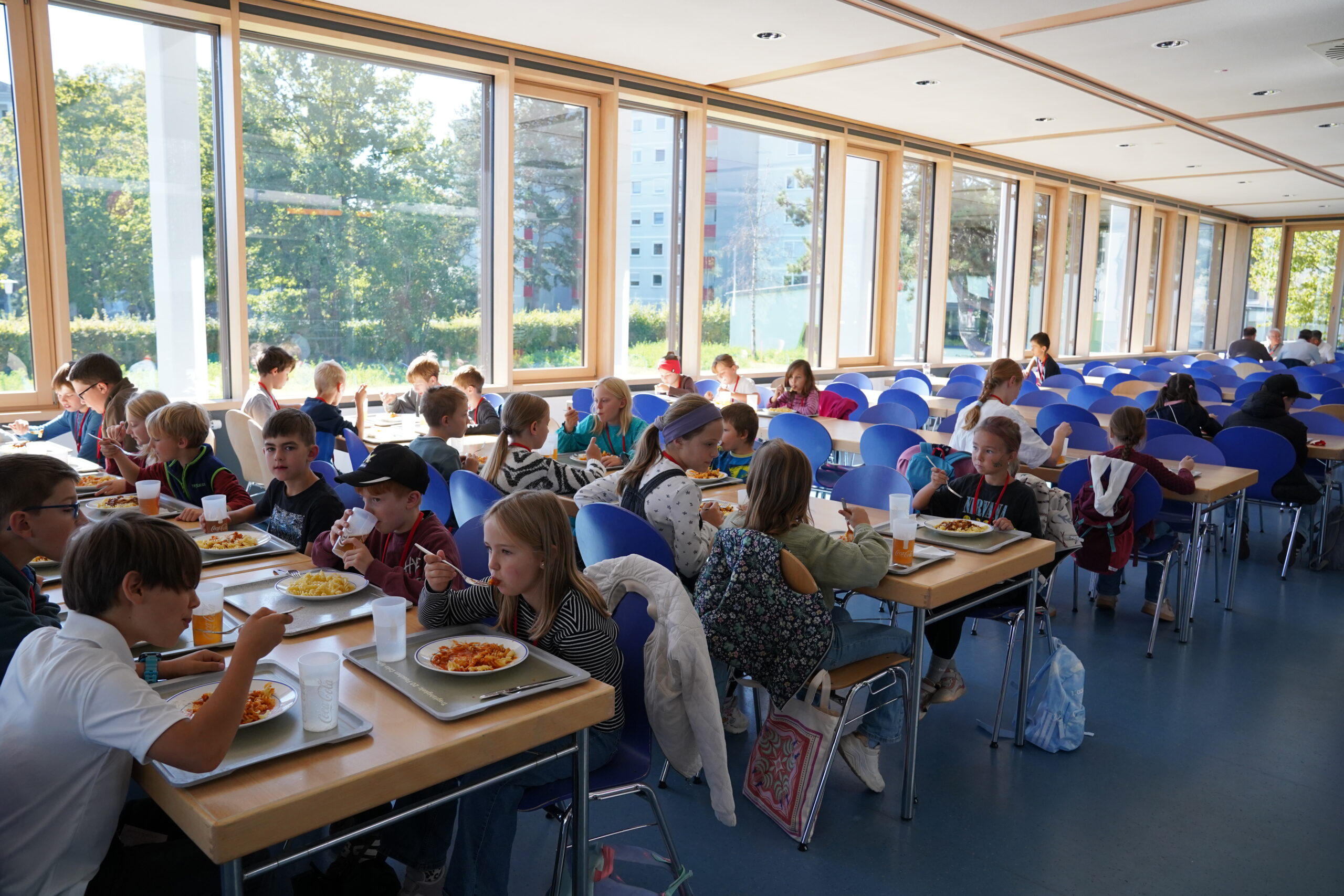 Kinder, die Stammgäste der KinderUni, sitzen an Tischen in einer hellen Cafeteria und essen zu Mittag. at Hochschule Coburg