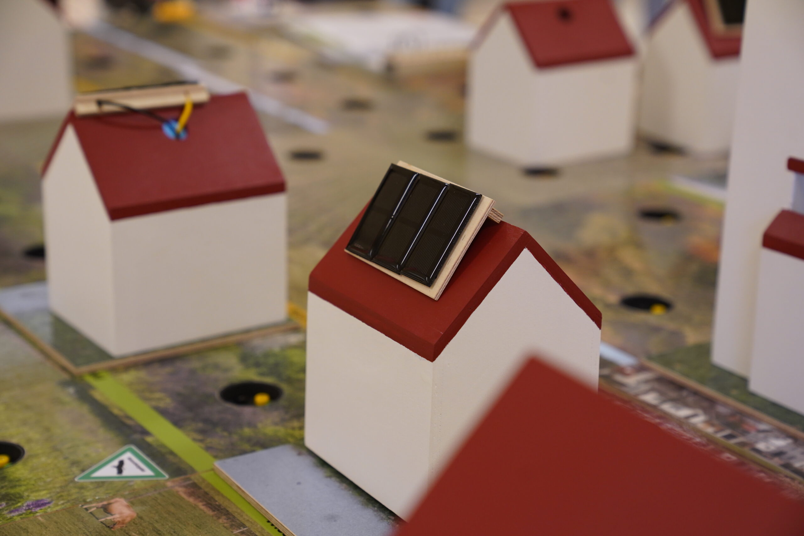 Kleine Modellhäuser mit roten Dächern und Solarmodulen, die auf einer Tischkarte für einen automatischen Entwurf ausgestellt sind. at Hochschule Coburg